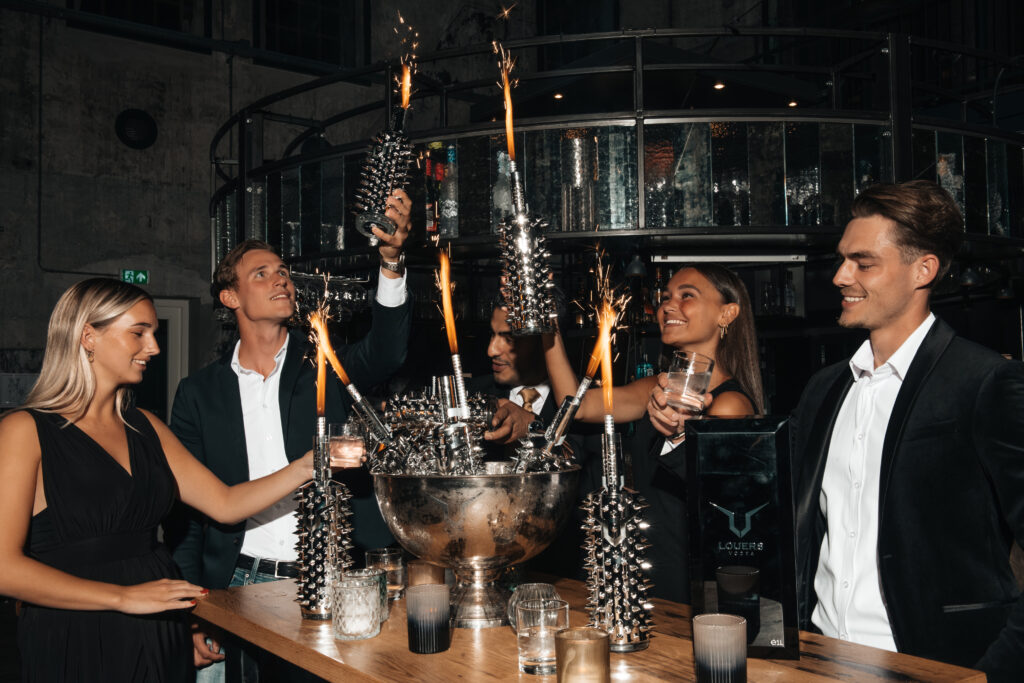 Grupka imprezujących osób wznosi toast wódką premium LOUERS