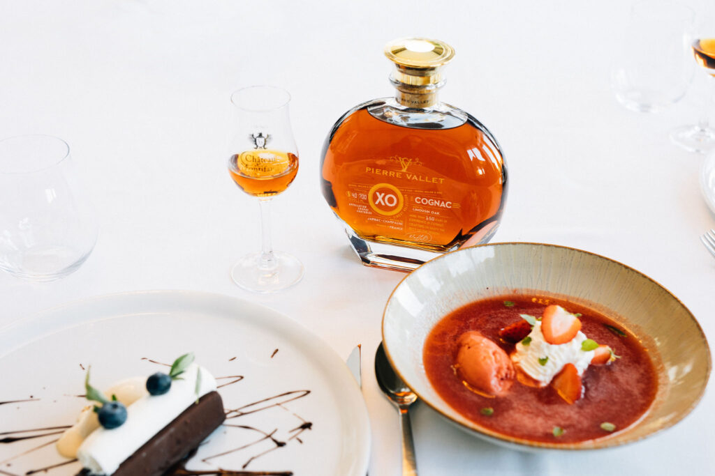A bottle of Pierre Vallet XO cognac along with a filled glass on the table, next to the desserts