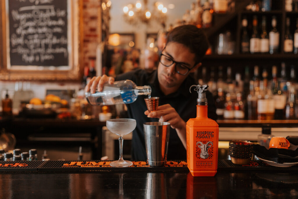 Barman nalewający wódkę do kieliszka w celu zrobienia koktajlu z likierem kawowym Jumping Goat, alkohol o smaku kawy, likier kawowy