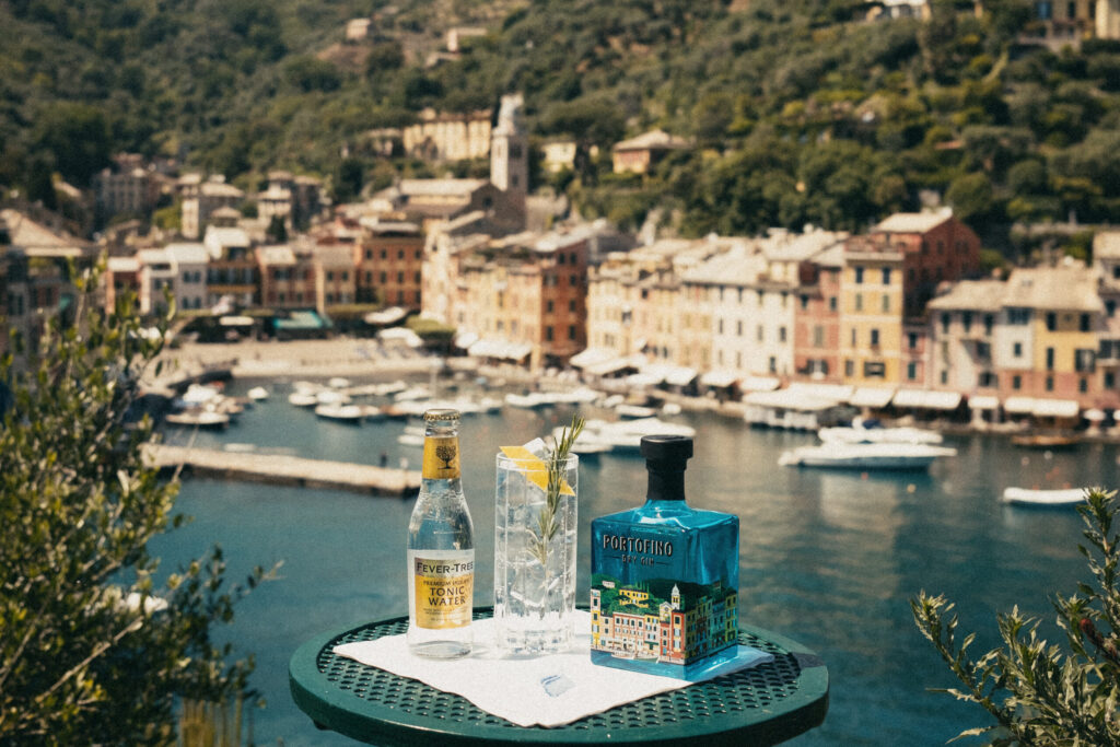 Butelka Portofino Dry Gin, obok szklanka z drinkiem Portofino z tonikiem, obok butelka toniku