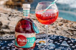 A bottle of Pampelle premium aperitif, next to a Pampelle brand wine glass with a straw, filled with the aperitif