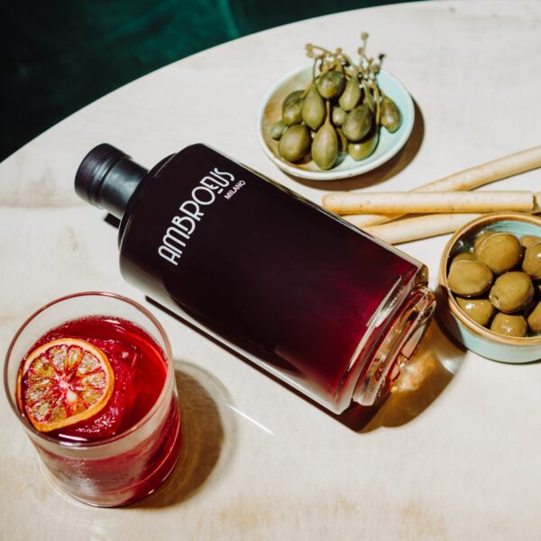 Butelka aperitifu bezalkoholowego Ambroeus na stole z oliwkami i drinkiem