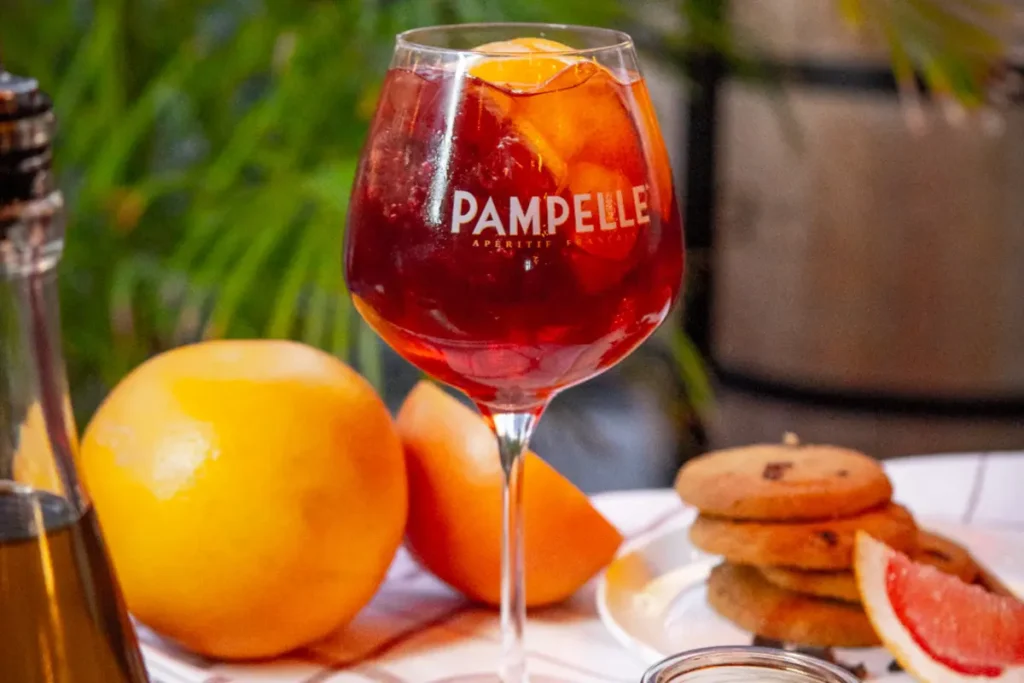 Pampelle and prosecco cocktail in an elegant glass with an orange slice, surrounded by fresh fruits and sweet treats.