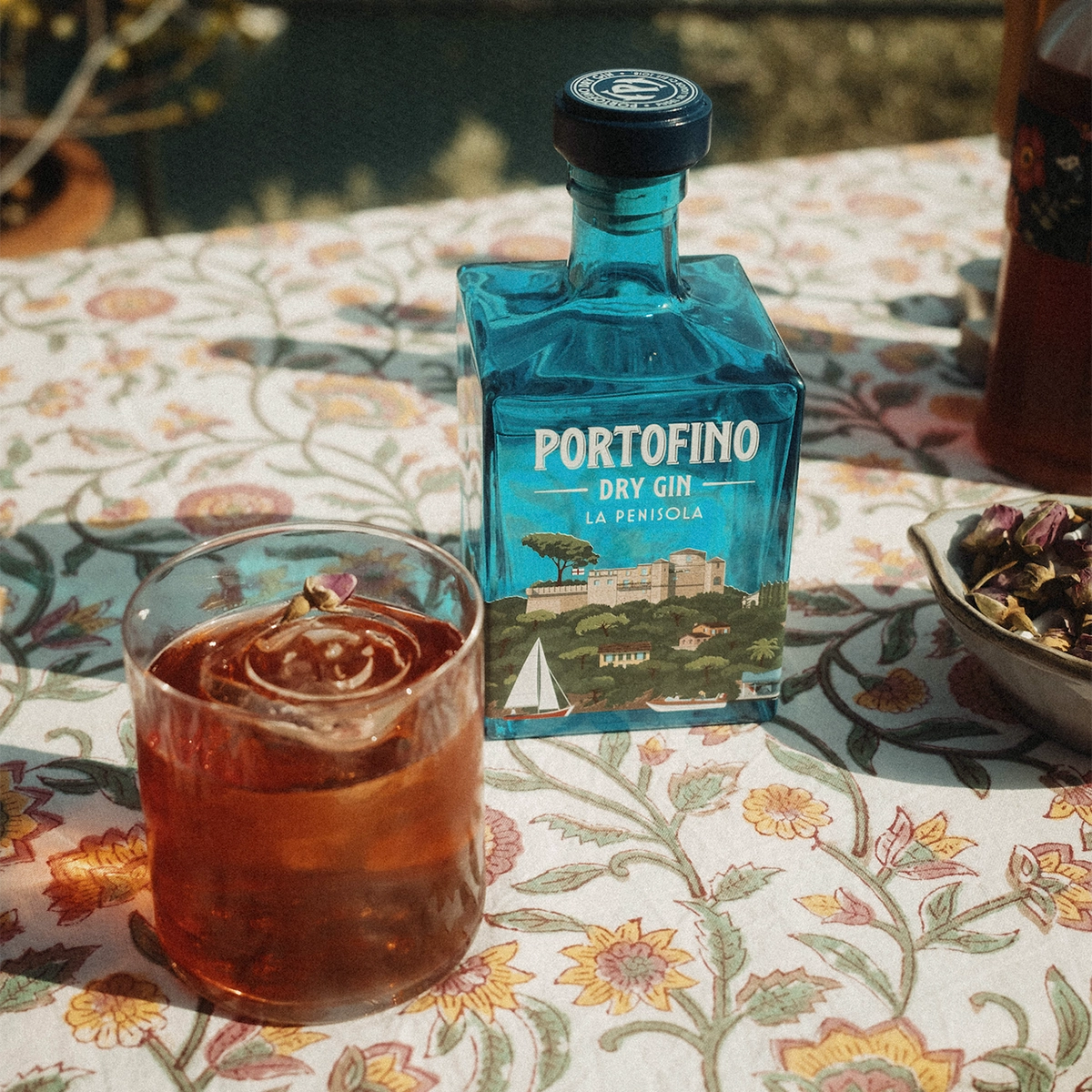 A bottle of Portofino Dry Gin La Penisola next to a glass with a drink.