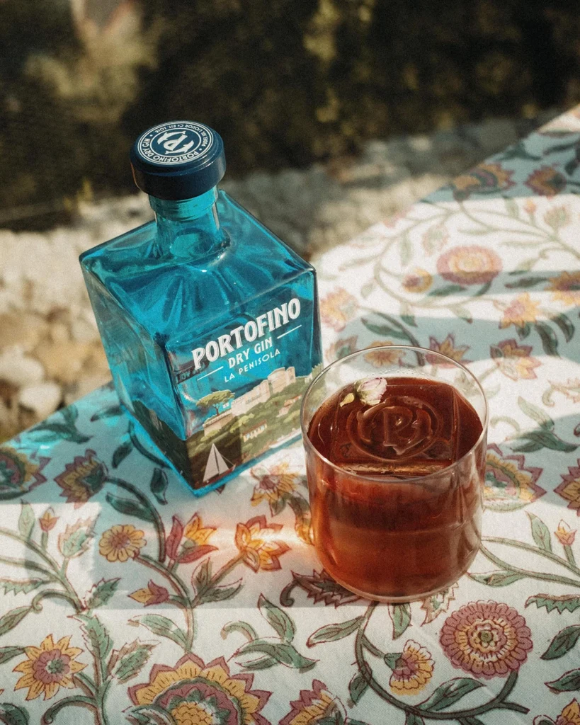 bottle of Portofino La Penisola gin next to a glass with a cocktail and a logo-stamped ice cube.