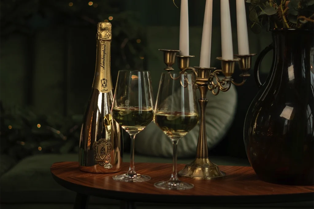 Luksusowe wino na prezent - złota butelka Lamborghini Prosecco Gold i dwa kieliszki na eleganckim stole.
