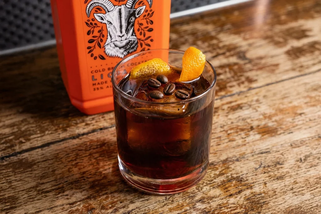 Coffee Negroni twist garnished with coffee beans and orange peel against the background of craft Jumping Goat liqueur.
