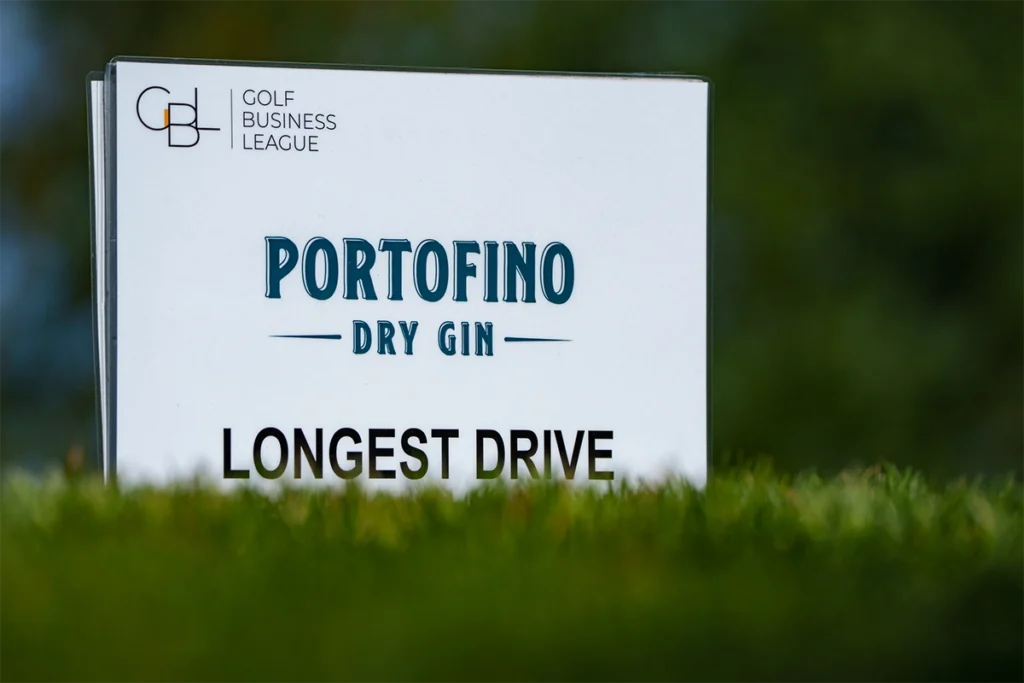 Tabliczka z napisem Portofino Dry Gin Longest Drive oraz logo turnieju Golf Business League, stojąca na zielonej trawie pola golfowego