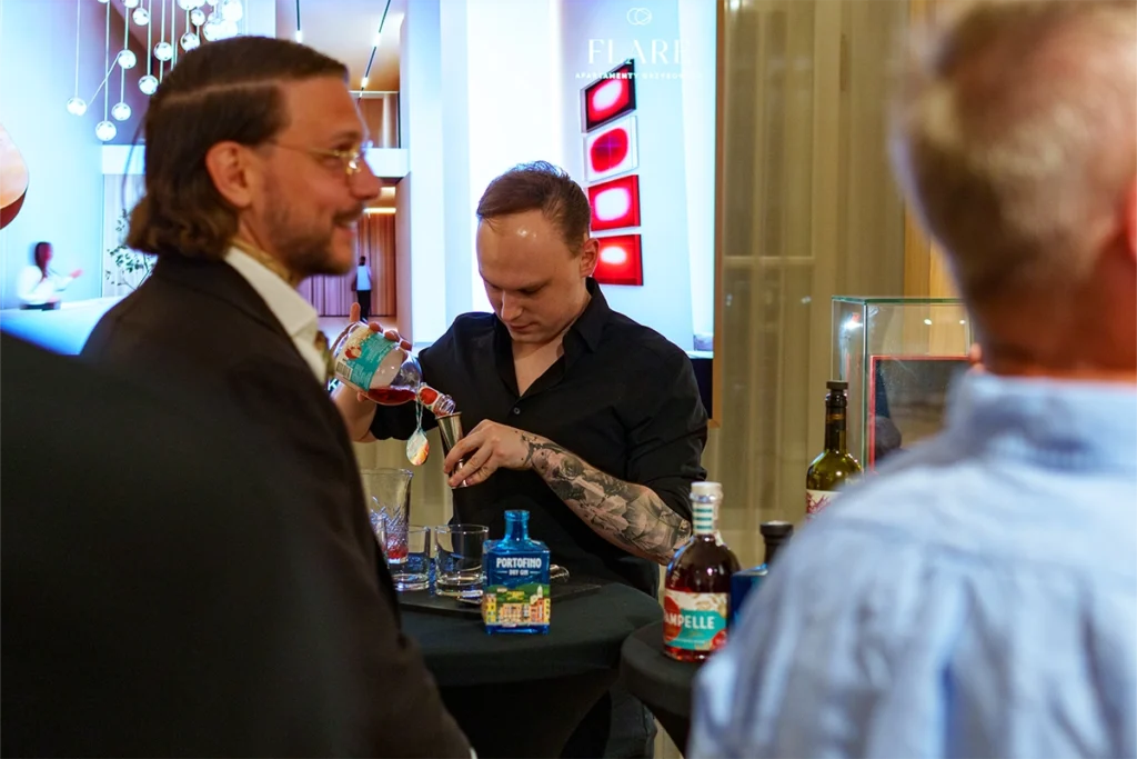 Barman w eleganckiej czarnej koszuli przygotowujący koktajle z butelki Pampelle podczas wieczornego bankietu po turnieju golfowym